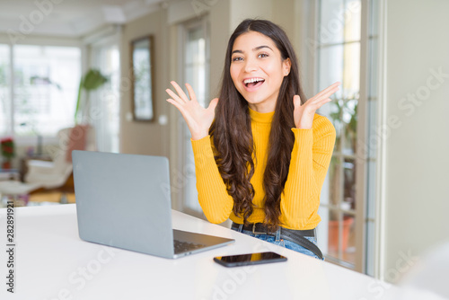 Young woman using computer laptop celebrating crazy and amazed for success with arms raised and open eyes screaming excited. Winner concept