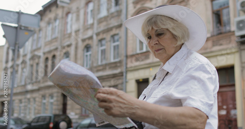 Senior female tourist exploring town with a map in hands. Looking for the route