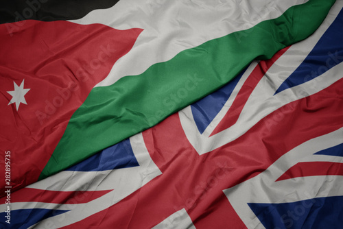 waving colorful flag of great britain and national flag of jordan.