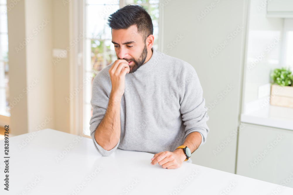 Handsome hispanic man wearing casual sweater at home looking stressed and nervous with hands on mouth biting nails. Anxiety problem. Handsome hispanic man wearing casual sweater at home looking stressed and nervous with hands on mouth biting nails. Anxiety problem.