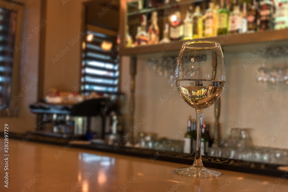 Glass of wine on bar counter in pub or restaurant. Bright blurred background with a coffee machine and glasses. Space for text