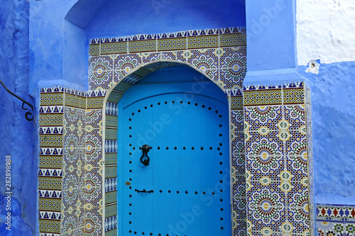 Decorated blue door surrounded by beautiful tiles in the medina of the blue city of Chefchaouen, Morocco, Africa