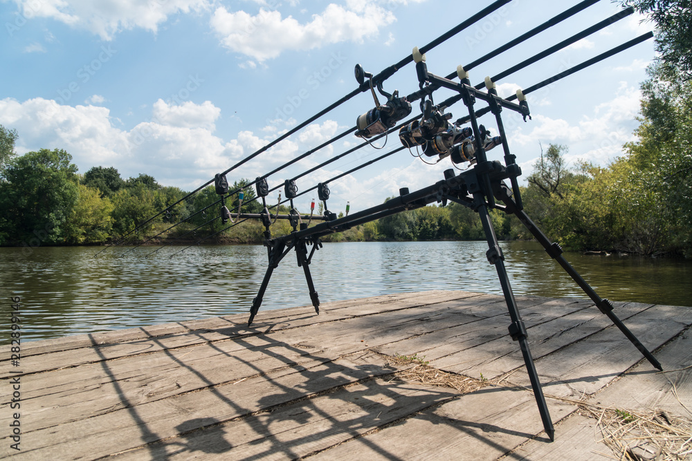 Carp fishing, rodpod with fishing rods on a wooden platform on the lake