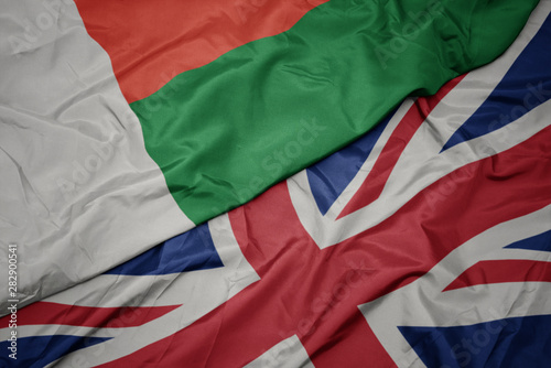 waving colorful flag of great britain and national flag of madagascar.