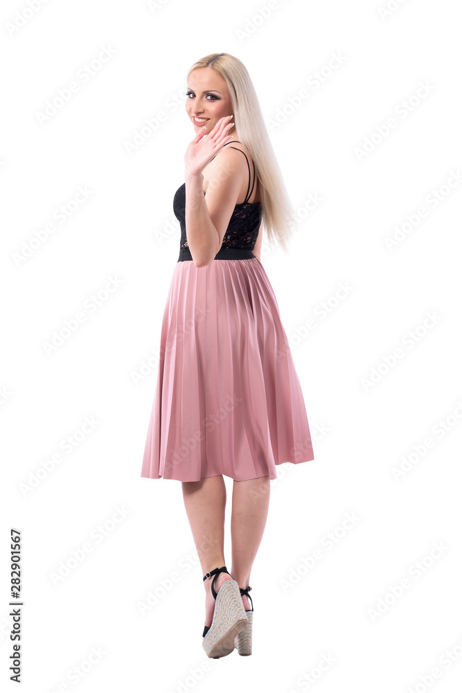 Back view of young blonde stylish woman in skirt walking away turning and waving hand goodbye to camera. Full body isolated on white background. 