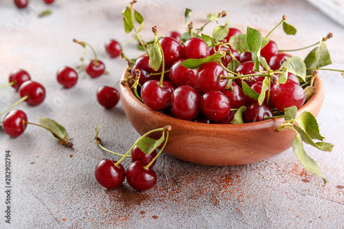 Fresh sweet cherries bowl with leaves on stone background, top view