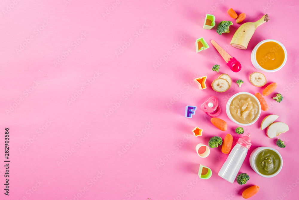 Infant baby food concept. Bowls with vegetable fruit puree, green, orange, yellow colors - broccoli, carrots, banana, apple. With baby accessories and toys pink background Flat lay top view copy space