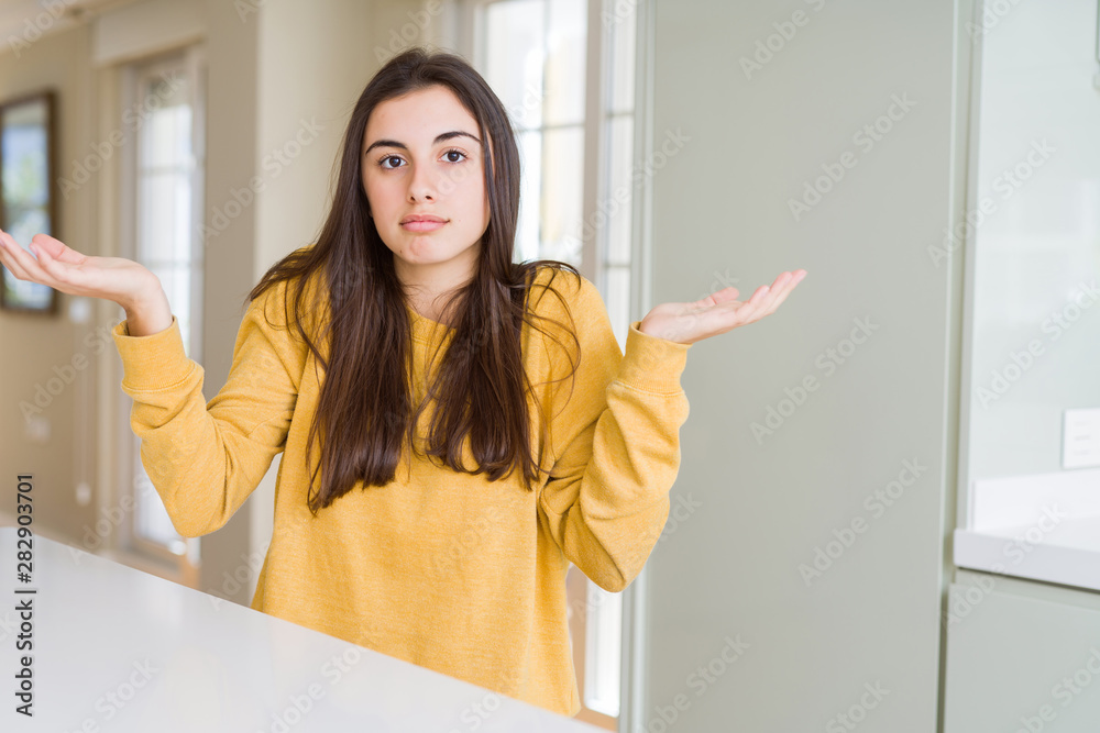 Beautiful young woman wearing yellow sweater clueless and confused expression with arms and hands raised. Doubt concept. Beautiful young woman wearing yellow sweater clueless and confused expression with arms and hands raised. Doubt concept.
