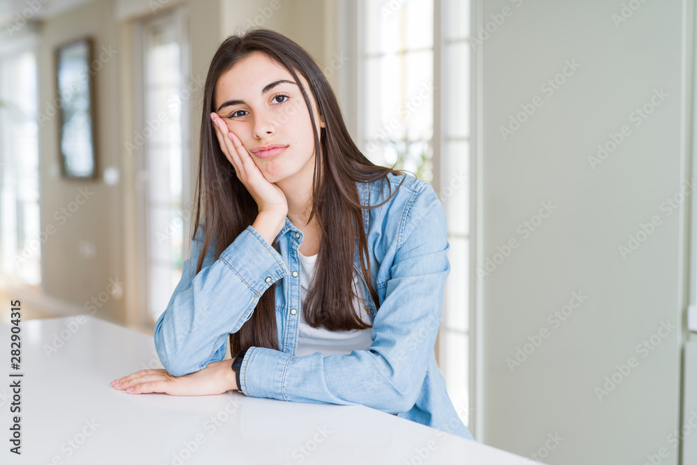 Beautiful young woman sitting on white table at home thinking looking tired and bored with depression problems with crossed arms. Beautiful young woman sitting on white table at home thinking looking tired and bored with depression problems with crossed arms.