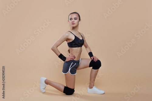 A young brunette girl standing on one knee. Knees protected by knee pads, on hands bandages. She prepared for training.