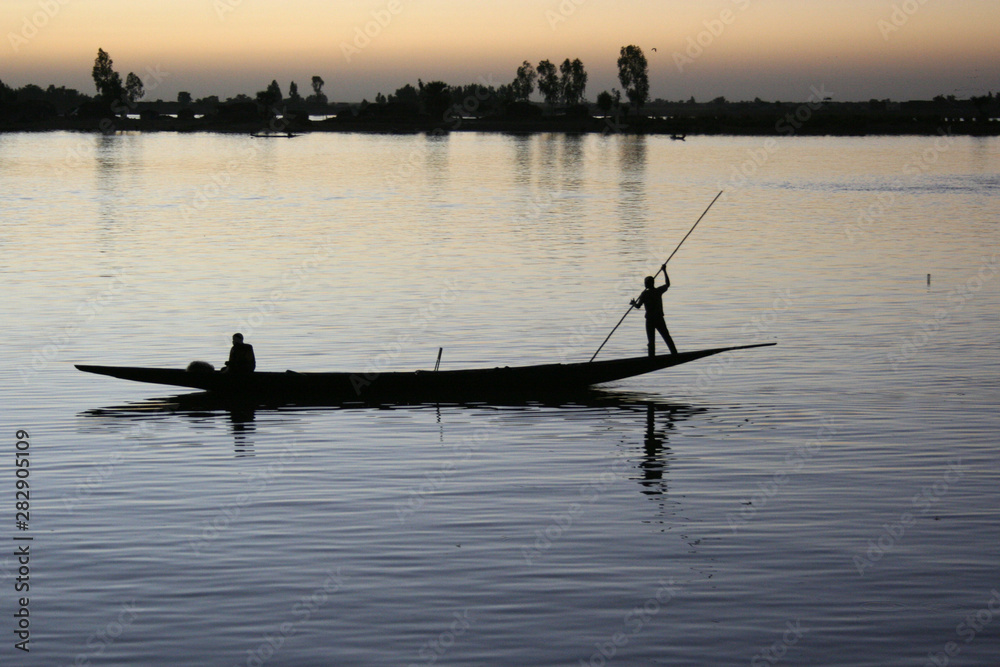 Naklejka premium A boat and its crew are silhouetted against the River Bani at dusk in Mopti, Mali on 8 December 2007