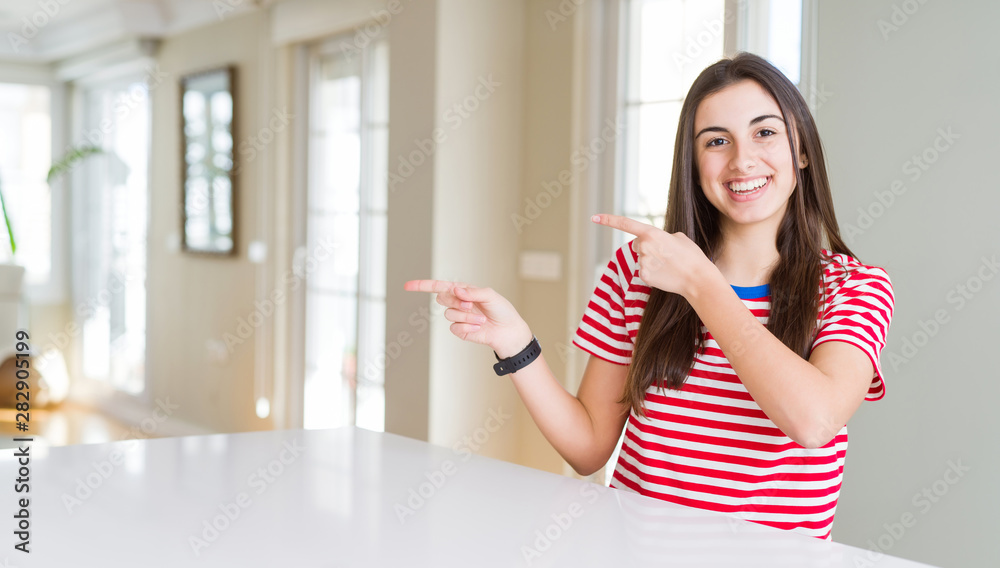 Beautiful young woman wearing casual stripes t-shirt smiling and looking at the camera pointing with two hands and fingers to the side.