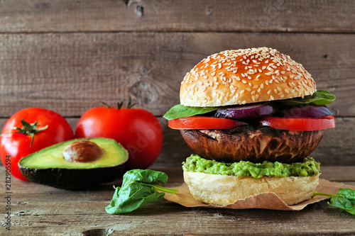 Portobello mushroom vegan burger with avocado, tomato, spinach and onion against a dark wood background