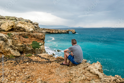  man sits on the edge of a cliff and looks into the distance at sea