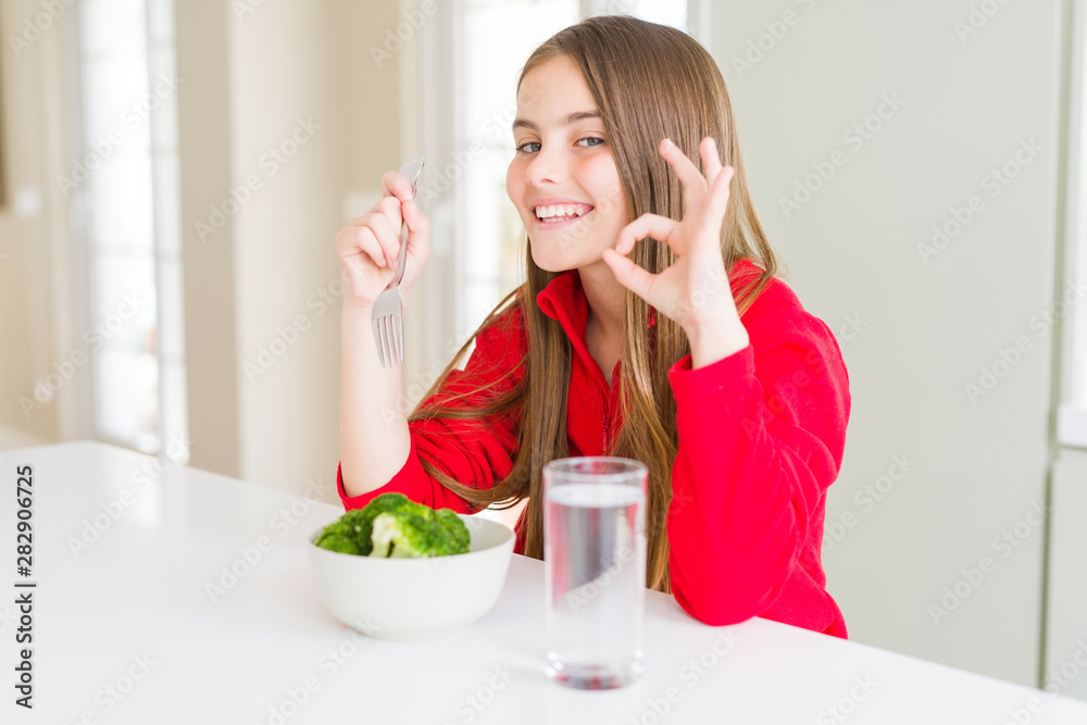 Beautiful young girl kid eating fresh broccoli and drinking water doing ok sign with fingers, excellent symbol Beautiful young girl kid eating fresh broccoli and drinking water doing ok sign with fingers, excellent symbol