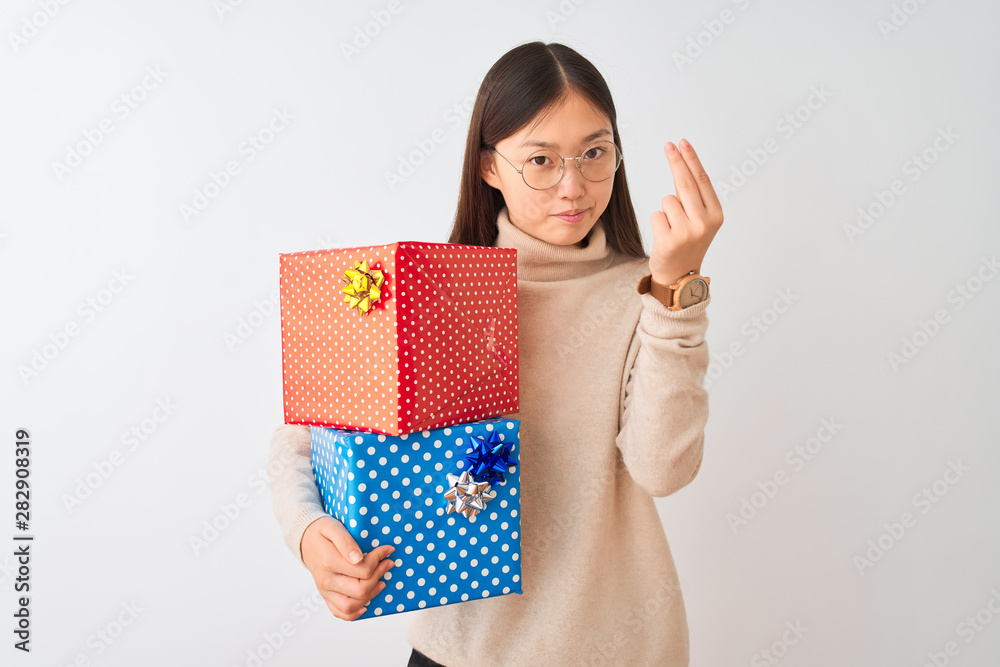 Young chinese woman holding birthday gifts over isolated white background Doing Italian gesture with hand and fingers confident expression