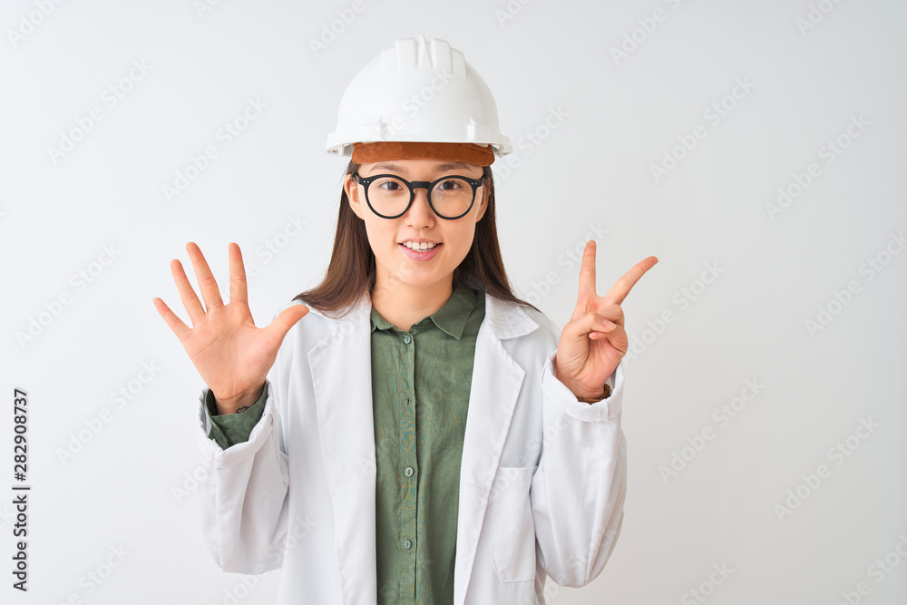 Young chinese engineer woman wearing coat helmet glasses over isolated white background showing and pointing up with fingers number seven while smiling confident and happy. Young chinese engineer woman wearing coat helmet glasses over isolated white background showing and pointing up with fingers number seven while smiling confident and happy.