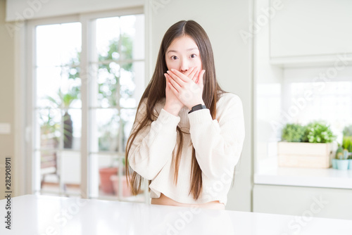 Beautiful Asian woman wearing casual sweater shocked covering mouth with hands for mistake. Secret concept.