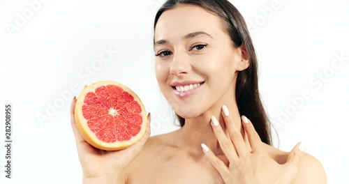 Attractive woman holding cutted half of grapefruit and touching skin, natural citrus cosmetics, bodycare