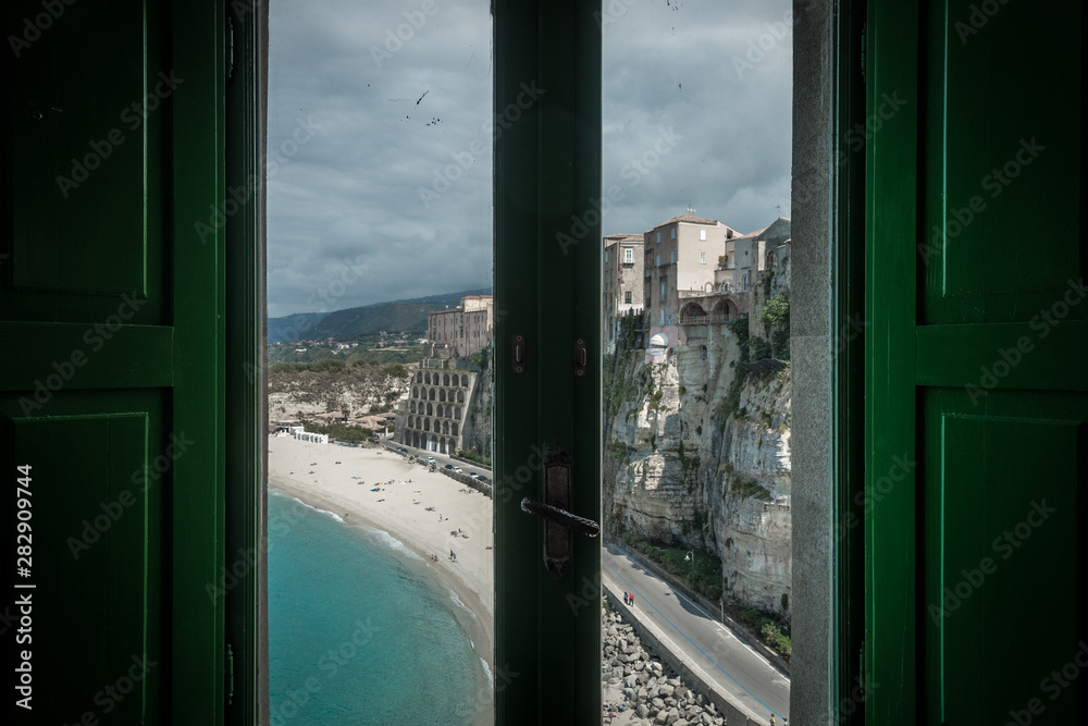An mix of buildings and rock on a beach front. The picture was made out of a window.