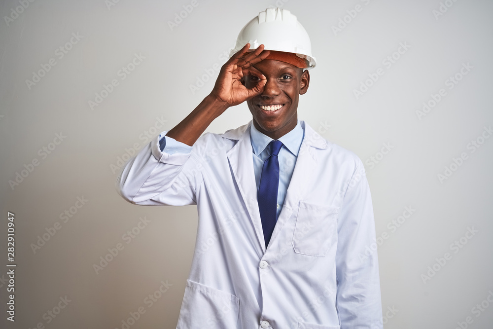 African american engineer man wearing coat and helmet over isolated white background doing ok gesture with hand smiling, eye looking through fingers with happy face. African american engineer man wearing coat and helmet over isolated white background doing ok gesture with hand smiling, eye looking through fingers with happy face.
