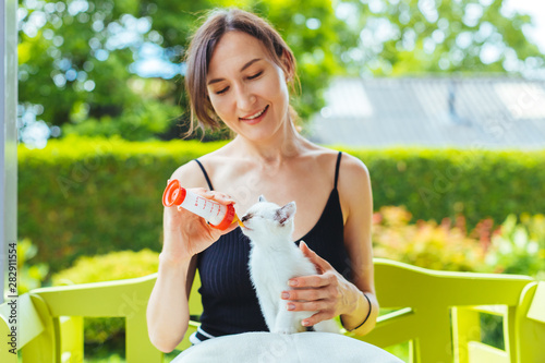 Valokuva Young smiling woman feeding with milk a white cute kitten from a bottle - growin