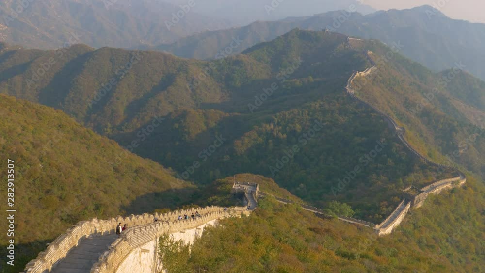 SLOW MOTION, DRONE: Flying above the Great Wall of China full of tourists observing the beautiful golden lit landscape. Stunning shot of the Great Wall crossing the forest covered mountains in China. SLOW MOTION, DRONE: Flying above the Great Wall of China full of tourists observing the beautiful golden lit landscape. Stunning shot of the Great Wall crossing the forest covered mountains in China.