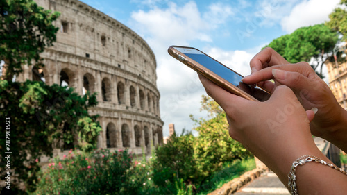 Photography Woman messaging on the smartphone with the Coliseum of Rome at background