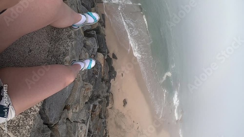 Female legs with a view of the Atlantic Ocean. Empty beach in Povoa de Varzim, Portugal on foggy autumn day with waves crashing on shore below and fog in distance. Vertical video frame 9:16. photo