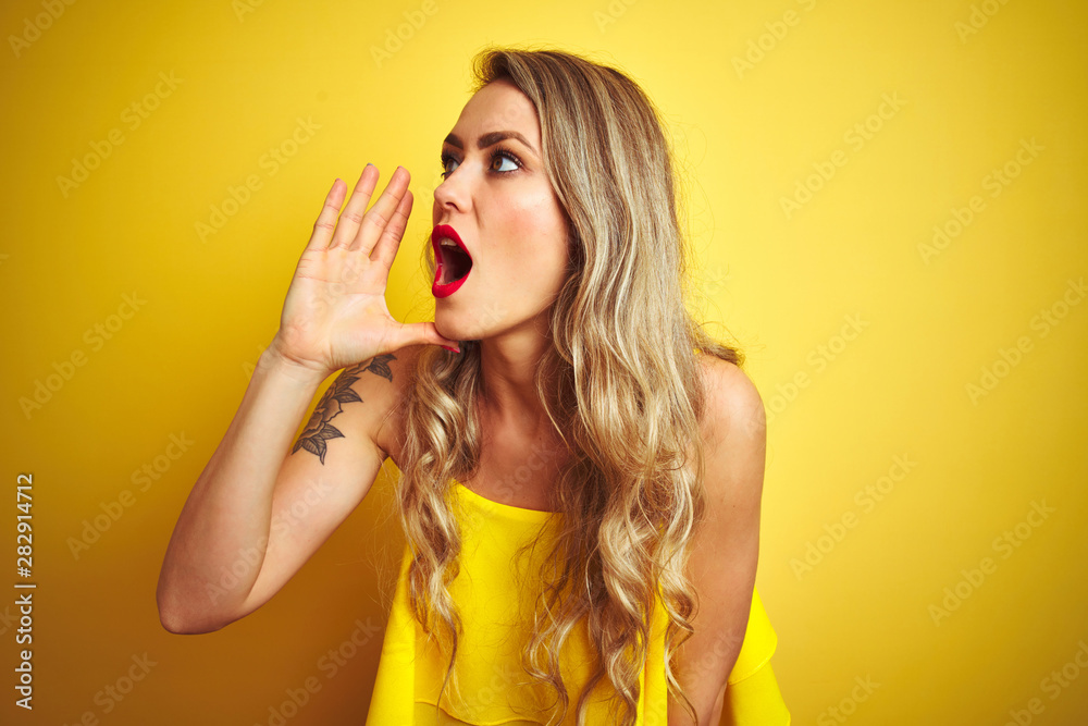 Young attactive woman wearing t-shirt standing over yellow isolated background shouting and screaming loud to side with hand on mouth. Communication concept. Young attactive woman wearing t-shirt standing over yellow isolated background shouting and screaming loud to side with hand on mouth. Communication concept.