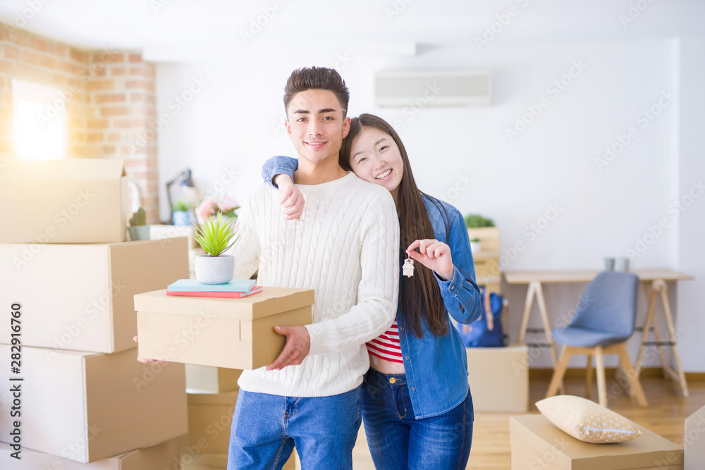 Fototapeta premium Young asian couple holding keys of new house, smiling happy and excited moving to a new apartment