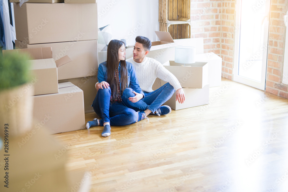 Young asian couple sitting on the floor of new house arround cardboard boxes relaxing and smiling happy Young asian couple sitting on the floor of new house arround cardboard boxes relaxing and smiling happy