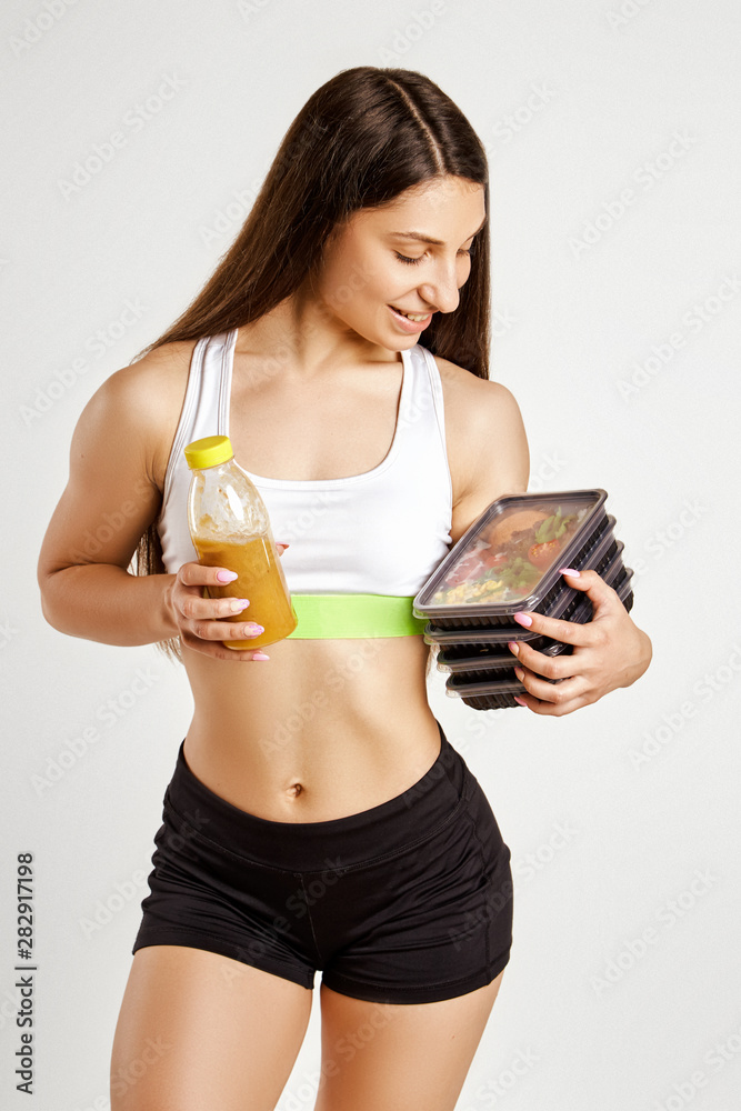 Beautiful muscular girl holds boxes with food and juice in a bottle.