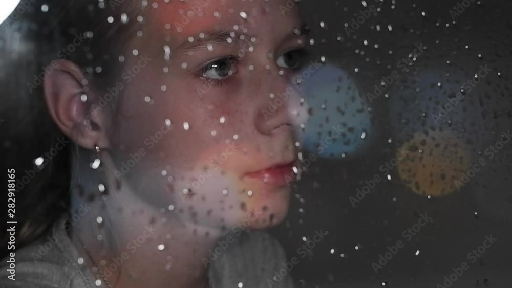 teenage girl looking out window with rain drops close-up view from outside teenage girl looking out window with rain drops close-up view from outside