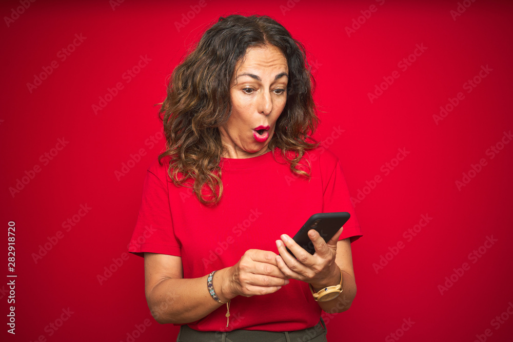 Middle age senior woman using smartphone over red isolated background scared in shock with a surprise face, afraid and excited with fear expression Middle age senior woman using smartphone over red isolated background scared in shock with a surprise face, afraid and excited with fear expression