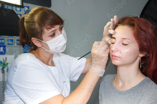 Beautician stains the client s eyebrows with a henna brush.
