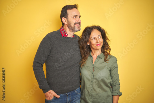 Beautiful middle age couple over isolated yellow background smiling looking to the side and staring away thinking.
