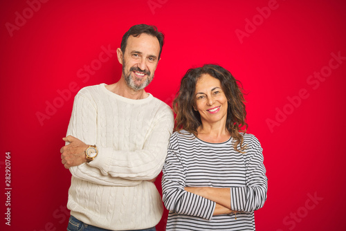 Beautiful middle age couple wearing winter sweater over isolated red background happy face smiling with crossed arms looking at the camera. Positive person.