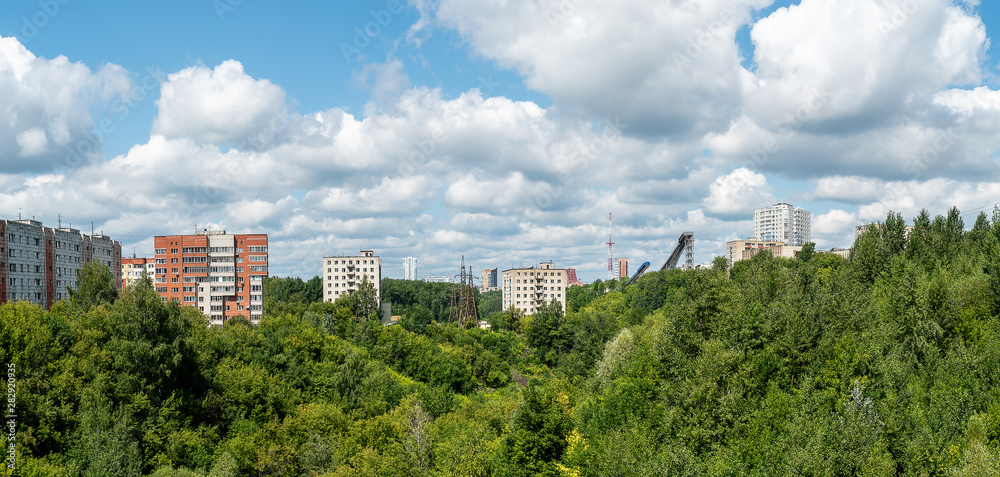In the foreground is a ravine, the slope of which is overgrown with trees and bushes. Along the slope of the ravine and away are multi-storey residential buildings. Perm, summer.