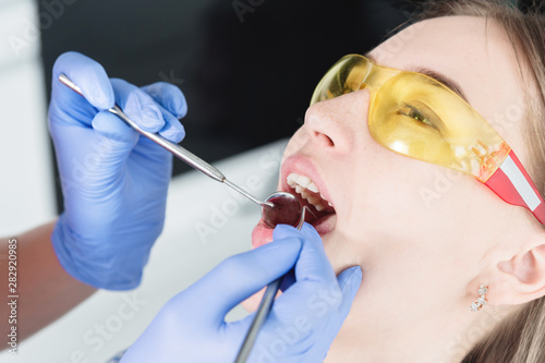 A close-up of the girl's face is examined by a dental examiner with his mouth open and a napkin and eyes closed. Dentist hands with inspection tools