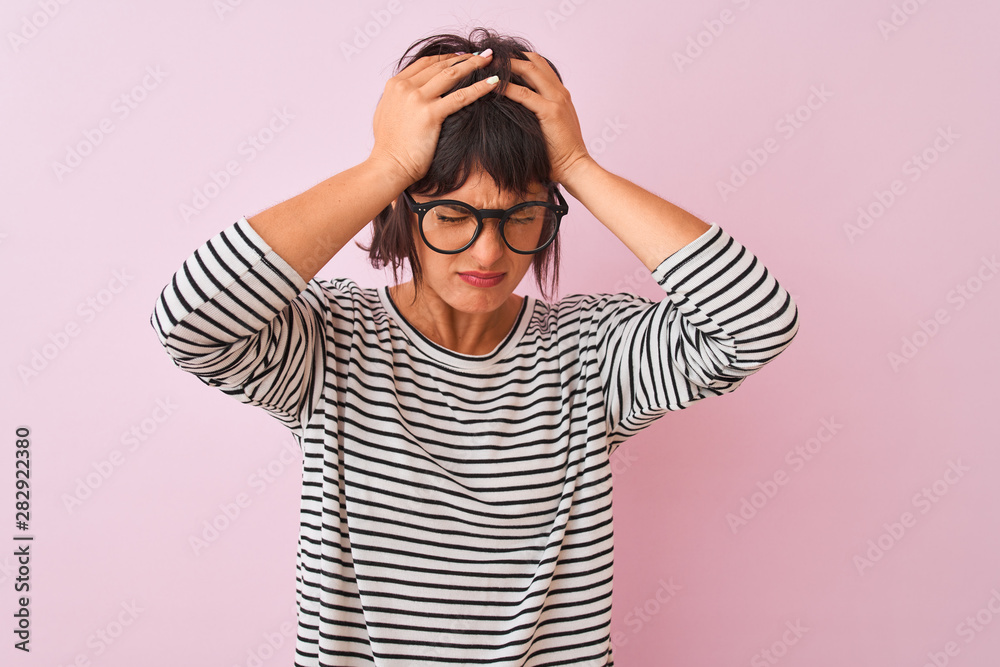 Young beautiful woman wearing striped t-shirt and glasses over isolated pink background suffering from headache desperate and stressed because pain and migraine. Hands on head. Young beautiful woman wearing striped t-shirt and glasses over isolated pink background suffering from headache desperate and stressed because pain and migraine. Hands on head.