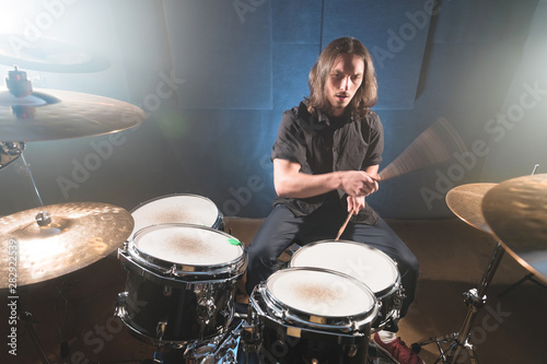 Portrait of a long-haired drummer with chopsticks in his hands sitting behind a drum set. Low key. Concepts of the creative freedom of the millenial generation