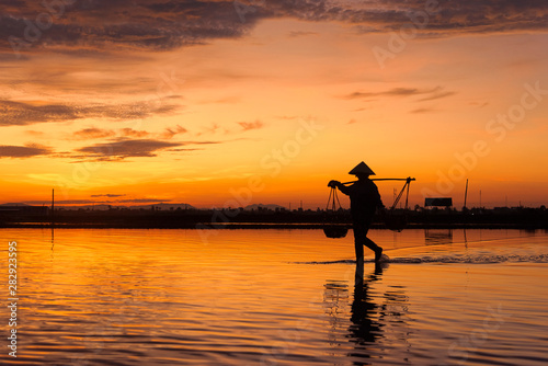 a woman carrying basket on the shoulder and preparing to harvest fresh salt at sunrise in Hon Khoi salt field, Nha Trang Province, Vietnam