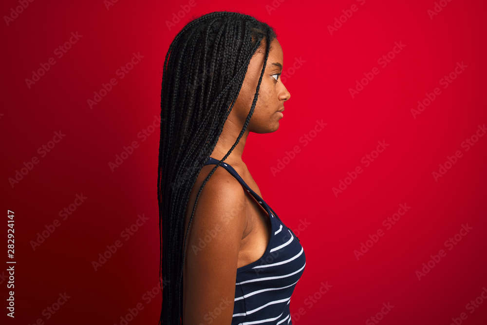 Naklejka premium Young african american woman wearing striped t-shirt standing over isolated red background looking to side, relax profile pose with natural face with confident smile.