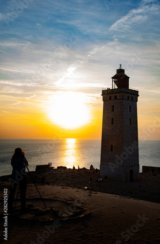 Image of professional female photographer taking pictures of a lighthouse at sunset on the North Sea