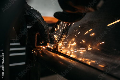 Industrial Worker with protective gloves welding motorcycle or car metal steel part at the factory workshop with a lot of sparks