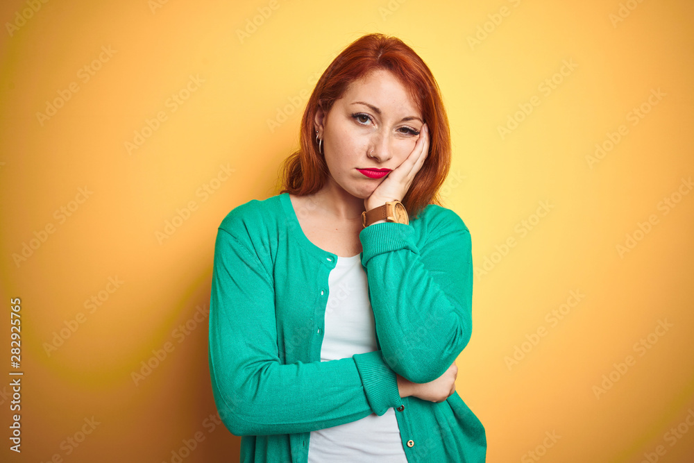 Youg beautiful redhead woman wearing winter green sweater over isolated yellow background thinking looking tired and bored with depression problems with crossed arms. Youg beautiful redhead woman wearing winter green sweater over isolated yellow background thinking looking tired and bored with depression problems with crossed arms.