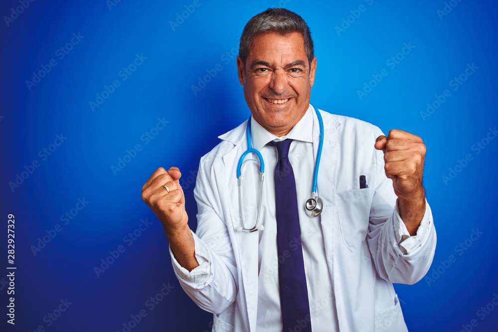Handsome middle age doctor man wearing stethoscope over isolated blue background very happy and excited doing winner gesture with arms raised, smiling and screaming for success. Celebration concept. Handsome middle age doctor man wearing stethoscope over isolated blue background very happy and excited doing winner gesture with arms raised, smiling and screaming for success. Celebration concept.