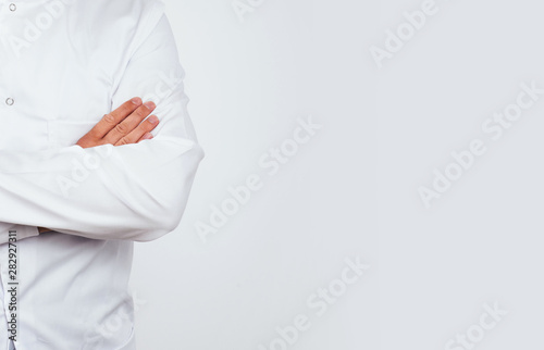 A man dressed in a white apron has crossed hands on a bright white background. Medical and pharmaceutical concept. A man dressed like a doctor. Preparation for the examination, health problems.