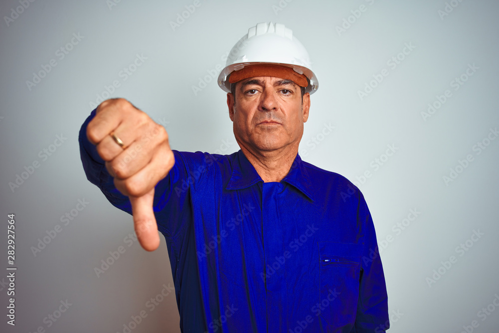 Handsome middle age worker man wearing uniform and helmet over isolated white background looking unhappy and angry showing rejection and negative with thumbs down gesture. Bad expression. Handsome middle age worker man wearing uniform and helmet over isolated white background looking unhappy and angry showing rejection and negative with thumbs down gesture. Bad expression.
